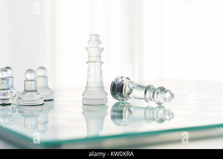 Un chiaro e un vetro smerigliato gioco di scacchi appena finito. Quella che il re si eleva alto mentre gli altri stabilisce nella sconfitta. Lo sfondo è bianco. Foto Stock