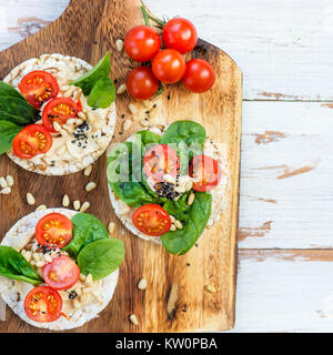 Snack sani da torte di riso con hummus, spinaci e pomodori in luce sullo sfondo di legno Foto Stock