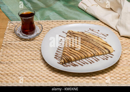 Piegate la crêpe, Russo blini con salsa di cioccolato su una piastra bianca servito con tè turco Foto Stock