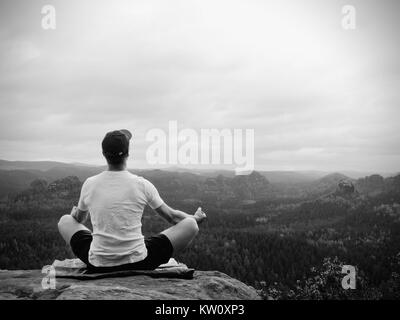 Solo l'uomo seduto a praticare Yoga pone su uno sperone roccioso a picco. L'uomo all'interno di foschia mattutina fare meditazione e gode di vista valle Foto Stock