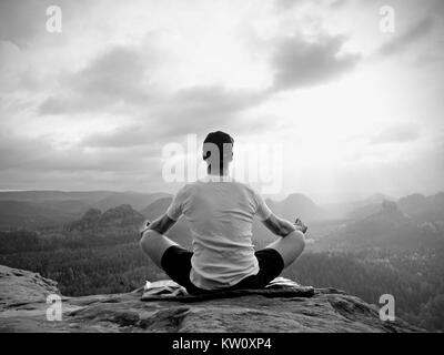 Solo l'uomo seduto a praticare Yoga pone su uno sperone roccioso a picco. L'uomo all'interno di foschia mattutina fare meditazione e gode di vista valle Foto Stock