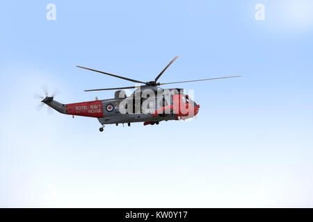Royal Navy Sea King elicottero su una esercitazione di soccorso sotto un vago blu cielo Foto Stock