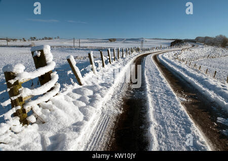 Coperta di neve torna su strada attraverso i terreni agricoli nei pressi di via, Lanarkshire, Scozia Foto Stock