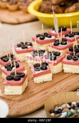 Crostini con olive nere, bianco formaggio e salame su un vassoio in legno Foto Stock
