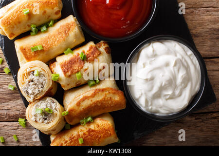 Crespelle con pollo e funghi close-up su un tavolo e salsa di pomodoro, panna acida. Parte superiore orizzontale vista da sopra Foto Stock