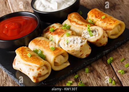 Frittelle rotoli farciti con pollo e funghi close-up e salsa di pomodoro, panna acida sul tavolo orizzontale. Foto Stock