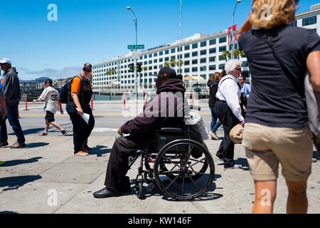 Nel bacino di Cina quartiere di San Francisco, California, un senzatetto si siede su una sedia a rotelle e chiede di cambiare passando da turisti, San Francisco, California, 2016. Foto Stock