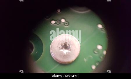 Luce di immagine al microscopio a circa 30x di ingrandimento che mostra un disco rigido la vite sul lato trasversale di una scheda a circuito stampato (PCB), 2016. Foto Stock