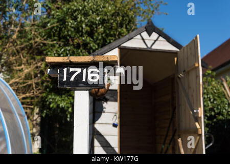 Un primo piano di un bellissimo dipinto di stile Tudor Tettoia da giardino in un giardino/riparto con un numero di legno posto di fronte ad esso un tress che lo circonda. Foto Stock