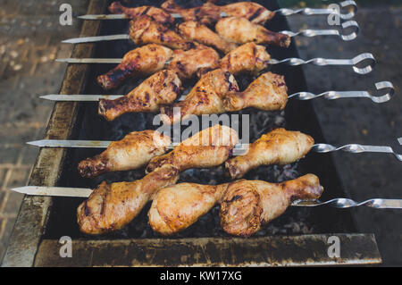 Pollo fritto gambe su spiedini tostata a carbone nella grande griglia. Primo piano. Carnosi bacchette di pollo con una deliziosa crosta croccante. Foto Stock