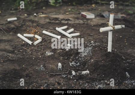 Una croce da butts. Il fumo uccide iscrizione die cui le sigarette per terra accanto alla tomba. Il concetto di anti-fumo. Foto Stock