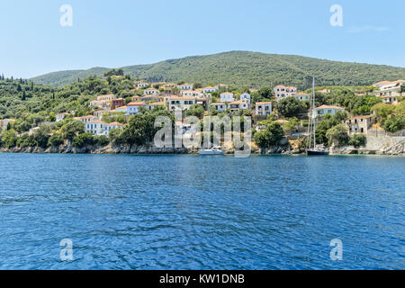 Sulle rive dell'isola greca di Ithika white case dipinte nestle tra alberi sulla collina mentre due barche sono ormeggiate vicino alla riva. Foto Stock