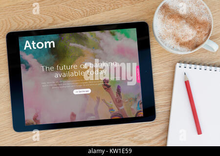 L Atomo Bank sito web su un iPad dispositivo tablet, appoggiato su un tavolo di legno accanto a un blocco note, matita e tazza di caffè (editoriale solo) Foto Stock