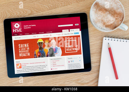 La salute e la sicurezza (HSE) sito su un tablet iPad appoggiato su un tavolo di legno accanto a un blocco note, matita e tazza di caffè (editoriale solo) Foto Stock