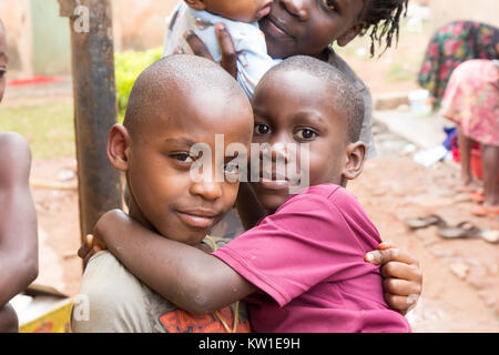 Lugazi, Uganda. 09 giugno 2017. Giovani ragazzi africani la tenuta dei loro fratelli nella loro armi. Le ragazze in background sono il lavaggio della biancheria in bacini. Foto Stock