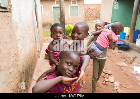 Lugazi, Uganda. 09 giugno 2017. Giovani ragazzi africani la tenuta dei loro fratelli nella loro armi. Le ragazze in background sono il lavaggio della biancheria in bacini. Foto Stock