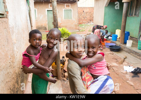 Lugazi, Uganda. 09 giugno 2017. Giovani ragazzi africani la tenuta dei loro fratelli nella loro armi. Le ragazze in background sono il lavaggio della biancheria in bacini. Foto Stock