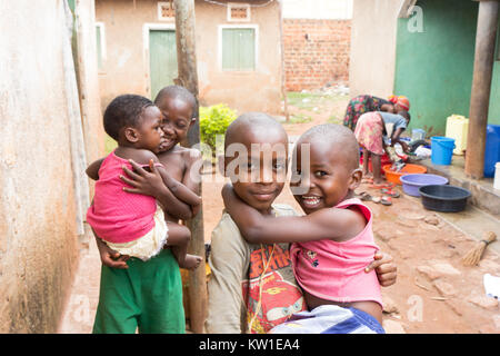 Lugazi, Uganda. 09 giugno 2017. Giovani ragazzi africani la tenuta dei loro fratelli nella loro armi. Le ragazze in background sono il lavaggio della biancheria in bacini. Foto Stock