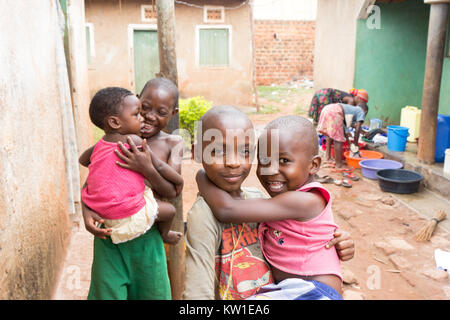 Lugazi, Uganda. 09 giugno 2017. Giovani ragazzi africani la tenuta dei loro fratelli nella loro armi. Le ragazze in background sono il lavaggio della biancheria in bacini. Foto Stock