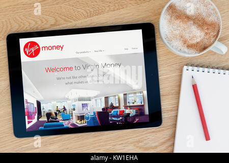 La Vergine denaro sito su un iPad dispositivo tablet pc che si appoggia su una tavola di legno accanto a un blocco note e matita e una tazza di caffè (editoriale solo) Foto Stock