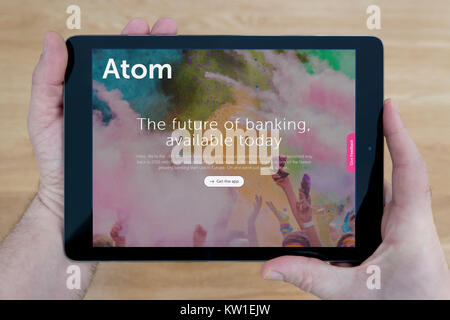 Un uomo guarda l'Atomo Bank sito sul suo iPad dispositivo tablet, sparato contro un tavolo di legno top sfondo (solo uso editoriale) Foto Stock
