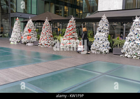 La donna che porta una borsa da shopping a camminare lungo una fila di artificiale alberi di Natale nel centro cittadino di Vancouver, BC, Canada Foto Stock
