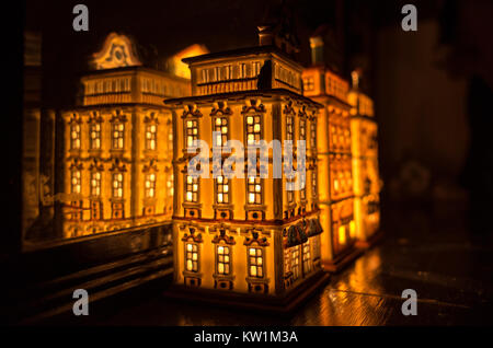 Un illuminato partylite tealight casa in miniatura su una superficie in legno nella parte anteriore dello specchio Foto Stock