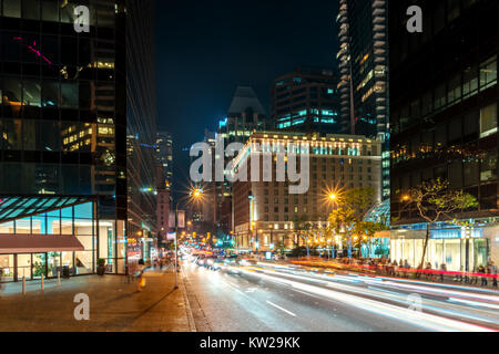 Notte estiva sulla strada di una grande città moderna con le alte case e la movimentazione di autovetture con fari accesi Foto Stock