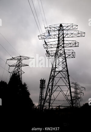 Silhouette di elecricity tralicci, cavi di alimentazione e cavi di telefono cellulare la torre contro un cielo grigio Foto Stock