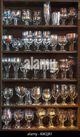 Assortimento di bicchieri da birra di diverse birre belghe visualizzata su scaffalature di legno nella caffetteria, Belgio Foto Stock