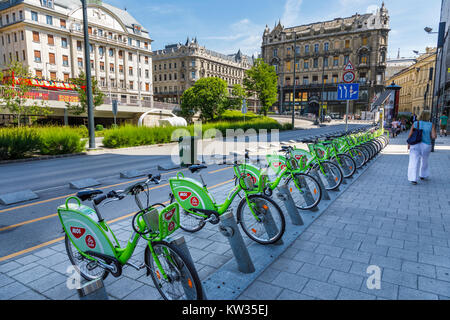 Riga di verde noleggio bici a noleggio schierate in rack a pagamento contro edifici storici di Pest Budapest, la città capitale di Ungheria, Europa centrale Foto Stock