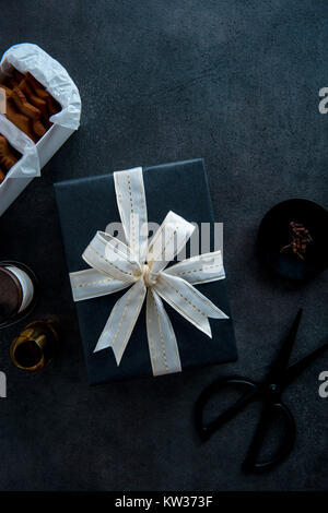 La confezione regalo per Natale. Vista superiore della tabella con il regalo in elegante carta nera con bianco e oro a nastro. Foto Stock