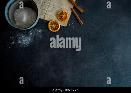 I biscotti di cottura nella cucina moderna. Ricetta impasto ingredienti (bastoncini di cannella, farina, essiccato fettine di arancia,) on dark tavolo moderno dal di sopra. Vista dall'alto. Foto Stock