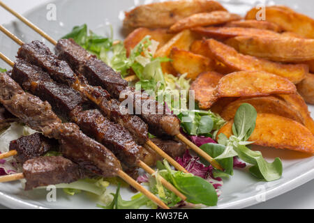 Spiedini di agnello su insalata con fette di patate e crema di latte Foto Stock