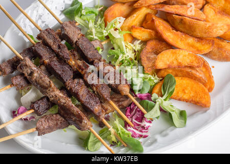 Spiedini di agnello su insalata con fette di patate e crema di latte Foto Stock