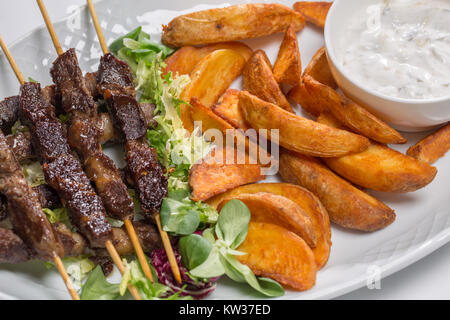 Spiedini di agnello su insalata con fette di patate e crema di latte Foto Stock