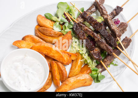 Spiedini di agnello su insalata con fette di patate e crema di latte Foto Stock