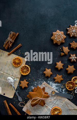 Vista superiore della preparazione di alimenti. A forma di stella di pan di zenzero i biscotti con la glassa e ingredienti (bastoncini di cannella, essiccato fettine di arancia, farina). Dark, moderno. Foto Stock