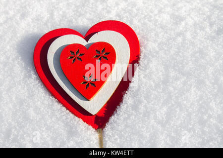 In caso di neve si trova un cuore rosso realizzato in legno. Modello per un holiday card con un bianco di consistenza e di spazio libero per il testo Foto Stock