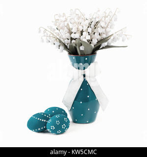 Uova pasquali dipinte di turchese e fiori di primavera in vaso corrispondente su sfondo bianco Foto Stock