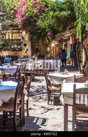 Tavoli da ristorante all'aperto in un soleggiato vicolo di pietra con fiori di bouganville nel centro storico di Chania Creta, Grecia Foto Stock