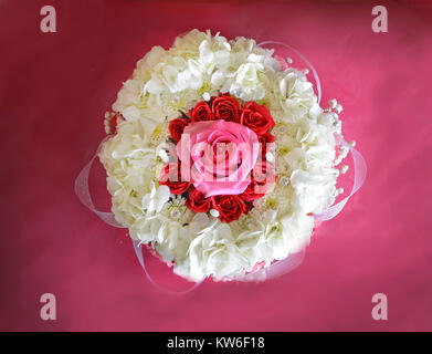 Vista panoramica di un matrimonio centrotavola di hydrangea bianco, rosso spray rose, nastri e perle che circonda una grande rosa rosa. Foto Stock