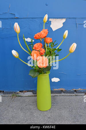 Tall disposizione di orange Rose e Tulipani in un vaso verde contro uno sfondo di spellatura della vernice blu. Foto Stock