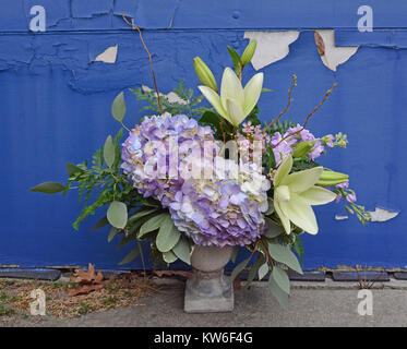 Vintage composizioni floreali contro un peeling sfondo blu. Ortensie e gigli in un urna di pietra. Foto Stock