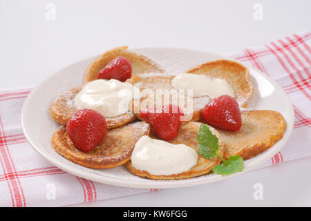 Piastra di piccole frittelle con panna montata e fragole - close up Foto Stock