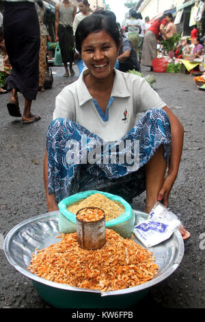 Donna con fiocchi di mais sul terreno, strada del mercato di Yangon, Myanmar Foto Stock