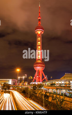 Oriental Pearl Tower - Una vista notturna di traffico pesante fluente passare la base di colore rossastro Oriental Pearl Tower presso il centro di Lujiazui, Pudong di Shanghai. Foto Stock