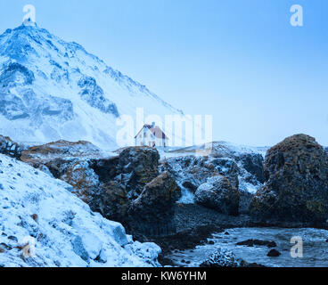 Casa solitaria dietro scogliere vicino al villaggio di Arnarstapi al tramonto in inverno, Snaefellsnes, Islanda. Foto Stock