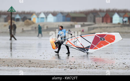 Un windsurf combatte contro il vento come egli cammina verso il mare sulla West Wittering beach in West Sussex. Foto Stock