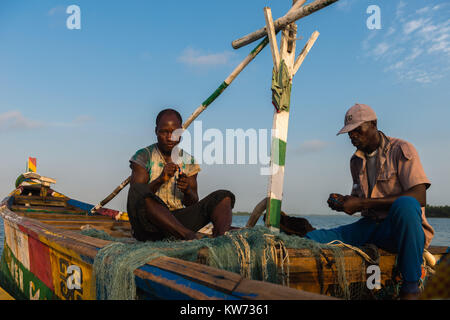 Fisherman riparare reti, seduto nella sua barca open, Volta River, Ada Foah, maggiore Regione di Accra, Ghana, Africa Foto Stock